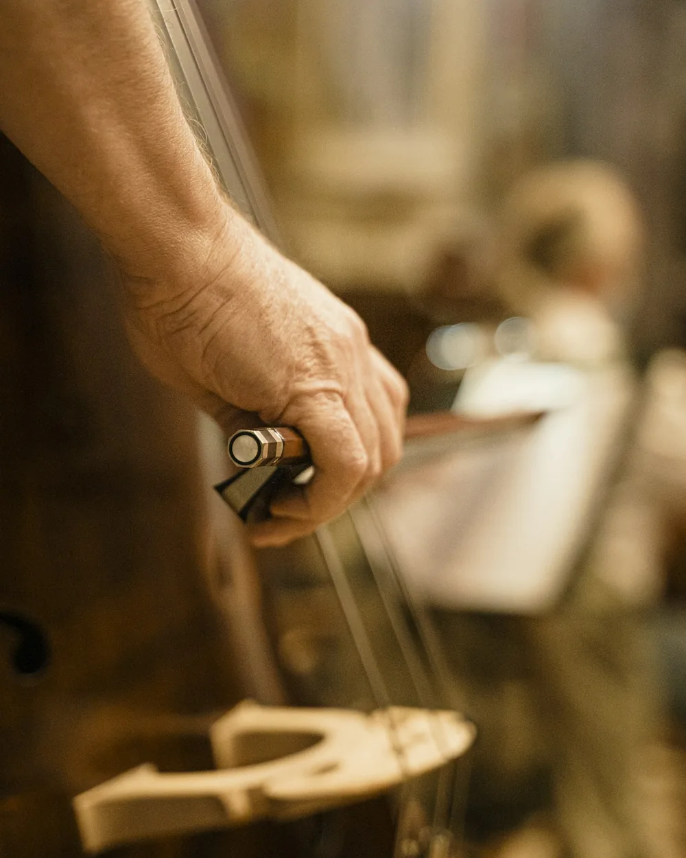 Manos sosteniendo una cuerda junto al mástil de un violín sobre el banco de trabajo